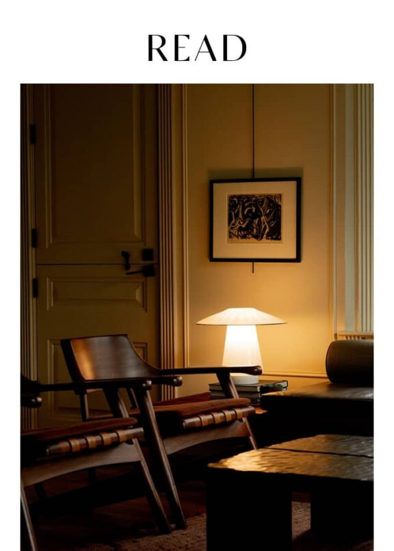 A warmly lit room with wooden chairs, a table lamp on a side table, framed artwork on the wall, and the word "READ" at the top.