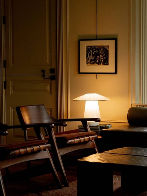 A warmly lit room with wooden chairs, a table lamp on a side table, framed artwork on the wall, and the word "READ" at the top.