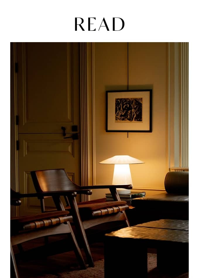 A warmly lit room with wooden chairs, a table lamp on a side table, framed artwork on the wall, and the word "READ" at the top.