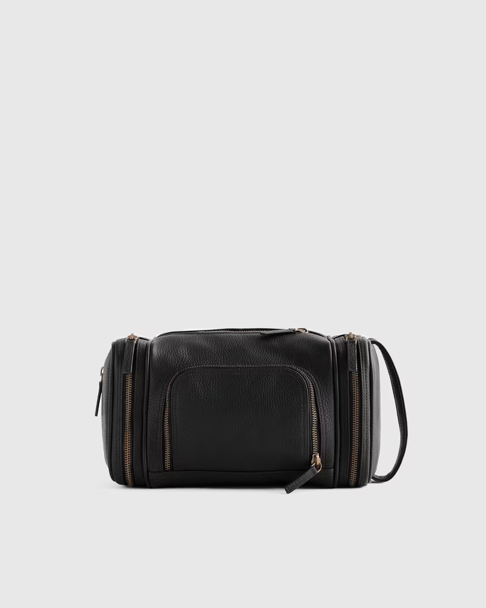 Black leather toiletry bag with multiple zippered compartments and a side carrying handle, photographed against a plain light gray background.