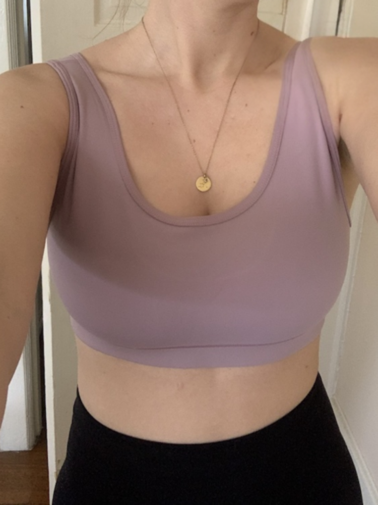 A person wearing a mauve sports bra and a gold necklace, photographed from the shoulders to the waist, standing indoors.