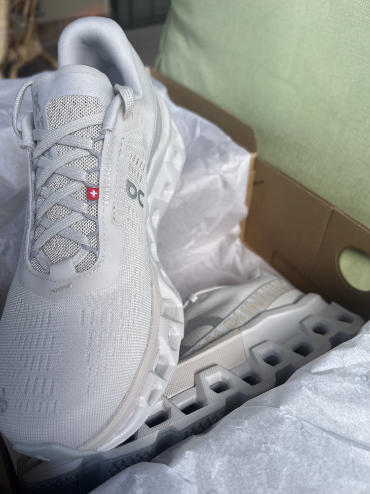 A pair of new white On running shoes in a shoebox, partially wrapped in tissue paper.