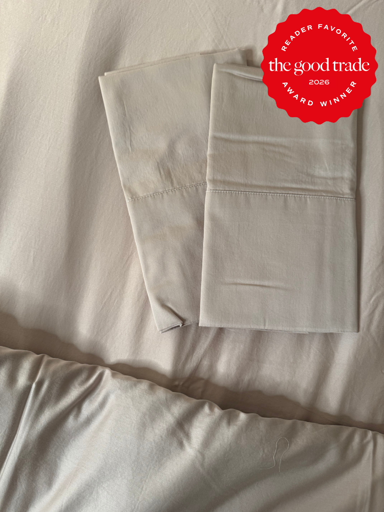 Two neatly folded cream-colored pillowcases on a matching bedsheet, with a red award badge in the corner that reads "The Good Trade, Reader Favorite, Award Winner 2026.