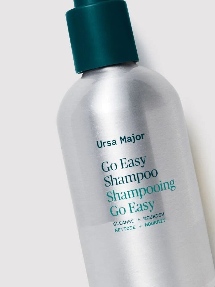 Clear bottle of Ursa Major Go Easy Shampoo with a pump top, next to text listing its benefits: gentle cleansing, moisture boost, healthy scalp, and creamy, sulfate-free lather.