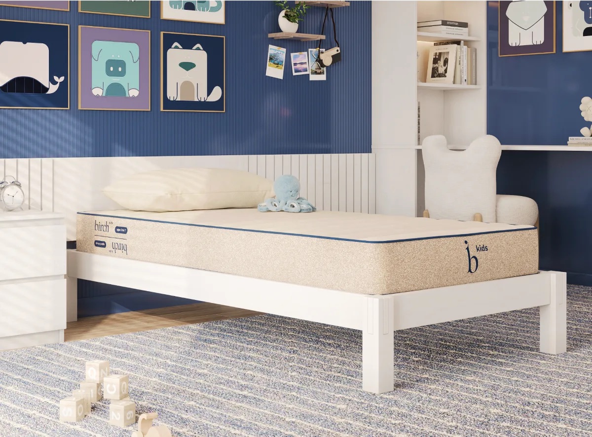 A neatly made single bed with a beige mattress in a children's bedroom, surrounded by blue-themed decor, wall art, and soft toys on a carpeted floor.