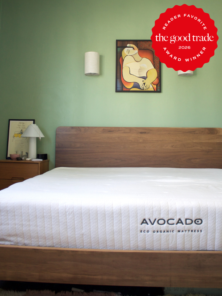 A neatly made bed with an Avocado eco organic mattress in a bedroom with green walls, modern wall lamps, and framed art, featuring a “Good Trade Award Winner 2026” badge.