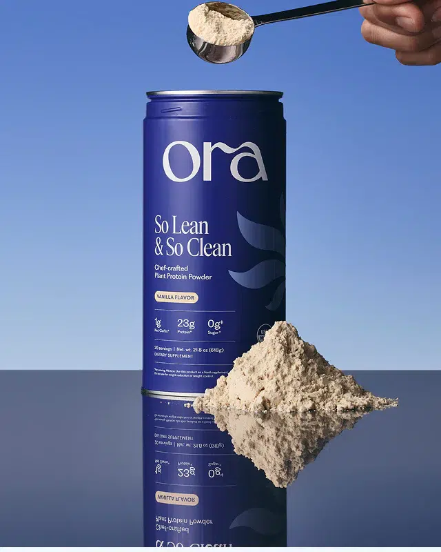 A blue Ora protein powder container labeled "So Lean & So Clean" sits next to a heap of powder, with a hand holding a scoop above them against a blue background.