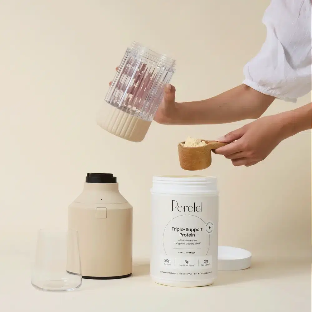 A person scoops protein powder from a container labeled "Perelel Triple-Support Protein" into a blender, with a glass placed nearby.