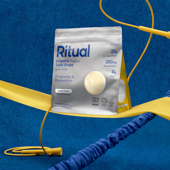 A Ritual Essential Protein Daily Shake pouch for pregnancy and postpartum is displayed among yellow jump ropes on a blue background.