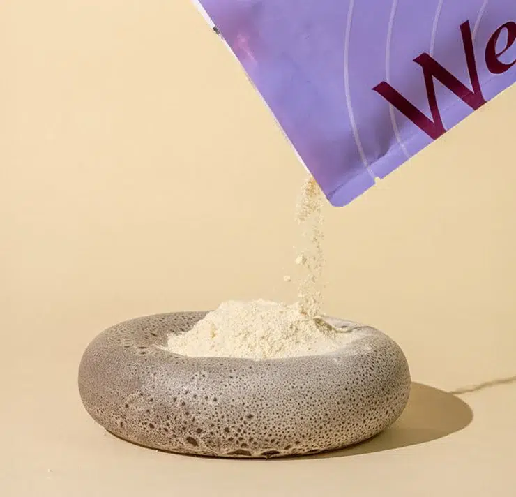A packet pours light-colored powder into a round, gray stone bowl against a beige background.
