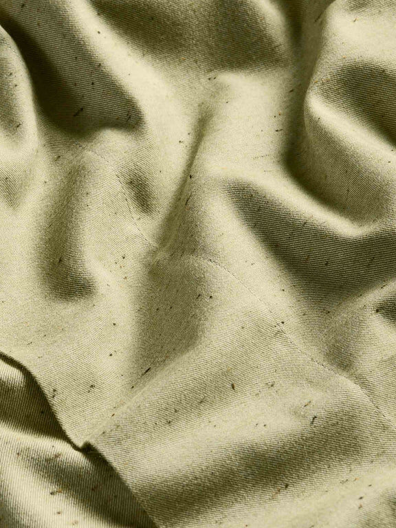 Close-up of wrinkled, light olive-green fabric with visible specks and texture.