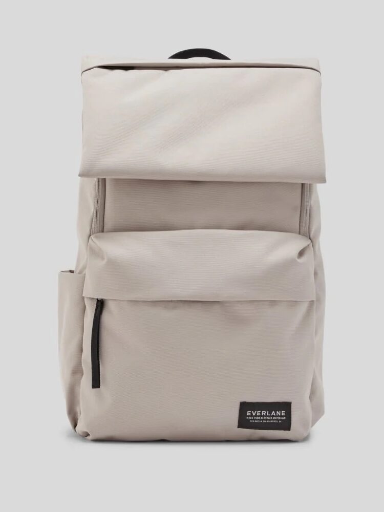 A light beige Everlane backpack with a front zipper pocket, side pocket, and top flap, displayed against a plain light background.