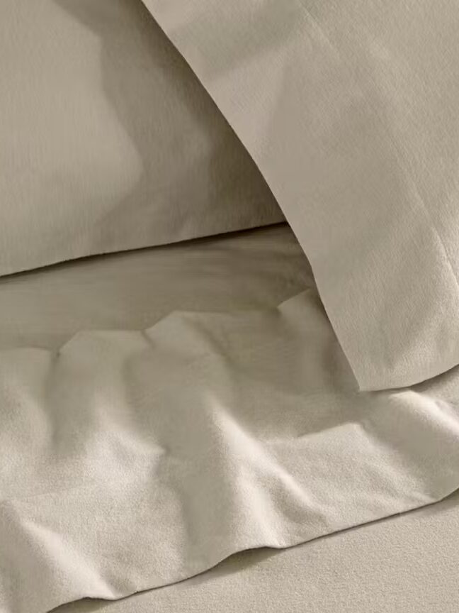 Close-up of beige bed sheets and pillowcases with a lightly wrinkled texture.