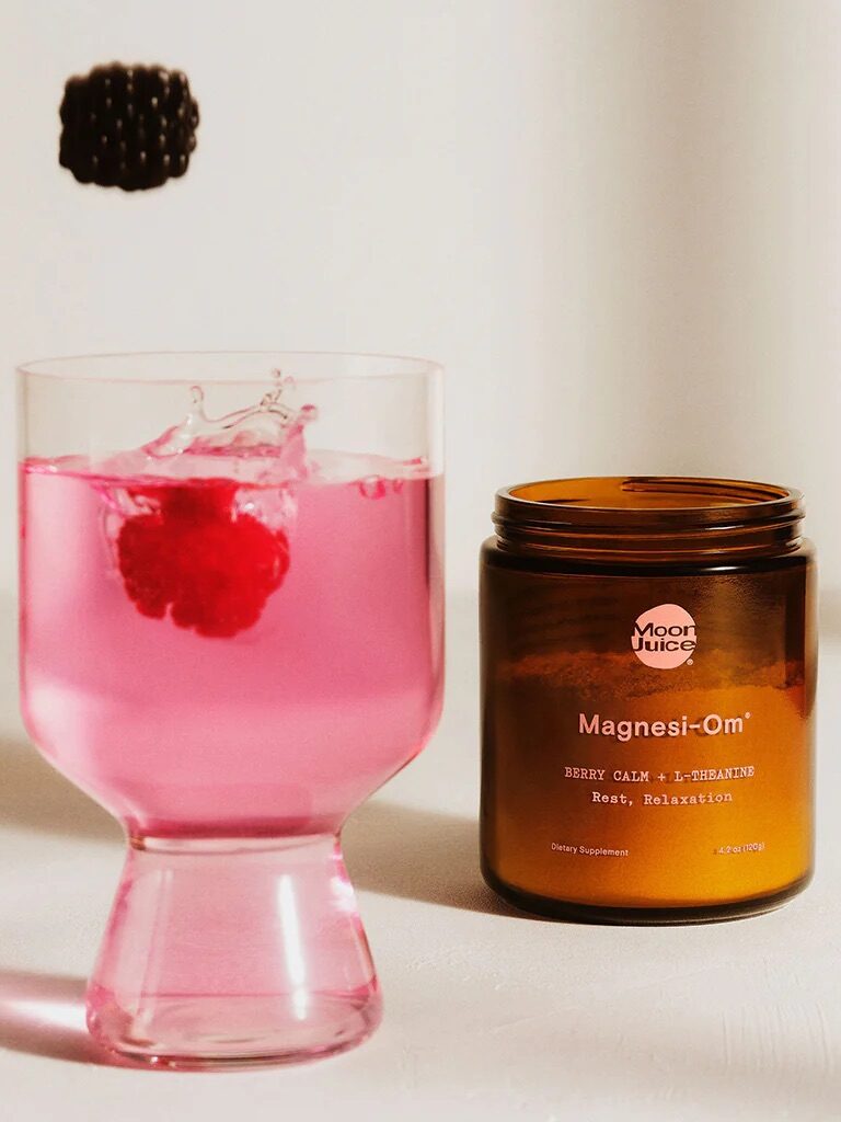 A blackberry drops above a pink drink with a raspberry inside, next to an open jar labeled "Moon Juice Magnesi-Om.