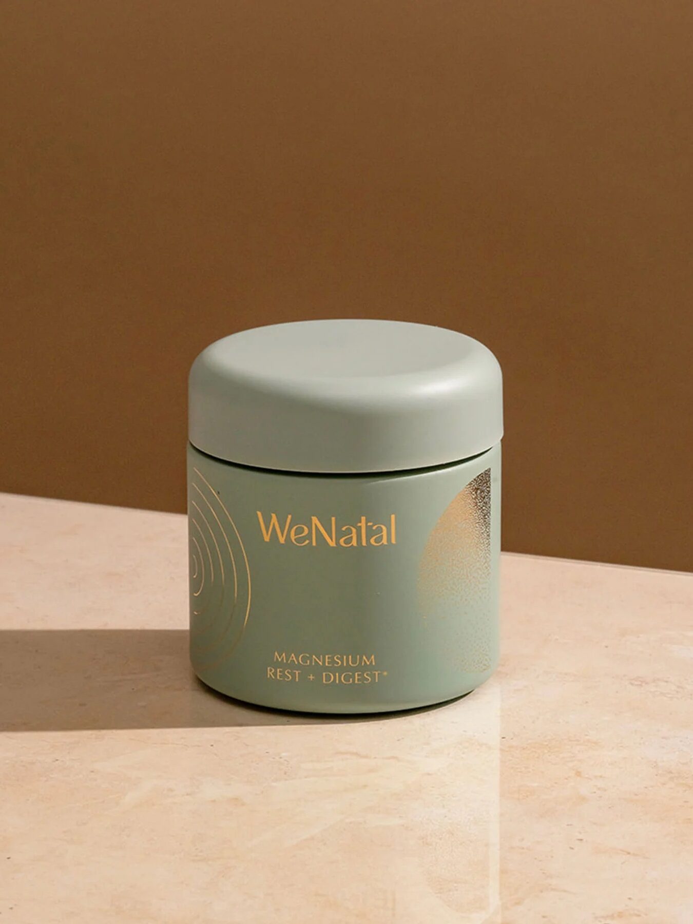 A green container labeled "WeNatal Magnesium Rest + Digest" sits on a beige surface against a brown background.