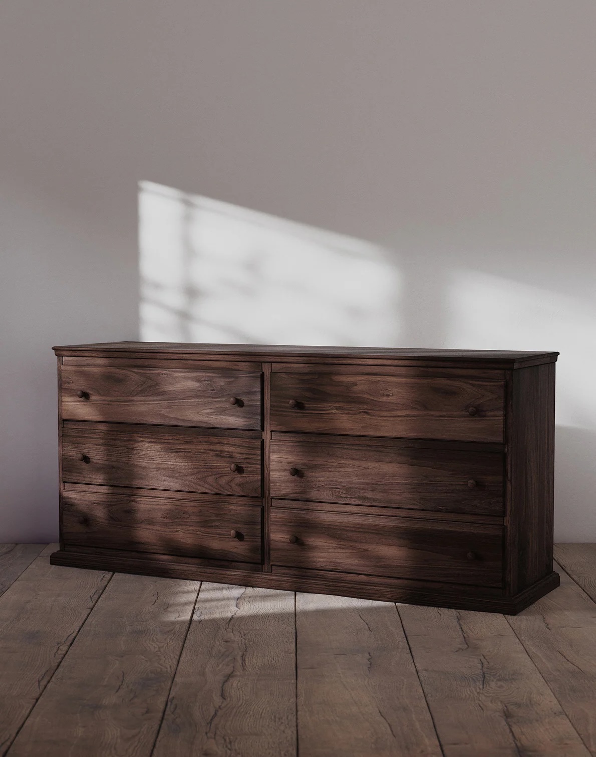 A dark wooden dresser with six drawers sits on a wooden floor against a plain white wall, with sunlight casting shadows on the wall.